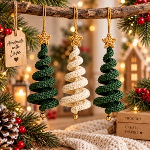 Può includere: Tre decorazioni natalizie a forma di albero all'uncinetto appese a un ramo. Due sono verde scuro e una è color crema, ciascuna sormontata da una piccola stella gialla all'uncinetto e una perlina dorata. Un'etichetta in legno riporta Handmade with Love.