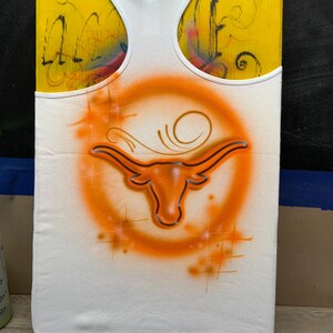 Peut inclure: D&eacute;bardeur blanc avec un logo Longhorn orange et un cercle orange. Le logo est peint &agrave; l'a&eacute;rographe sur le tissu. Le d&eacute;bardeur a une bordure blanche et un dos nageur. Le fond est jaune.