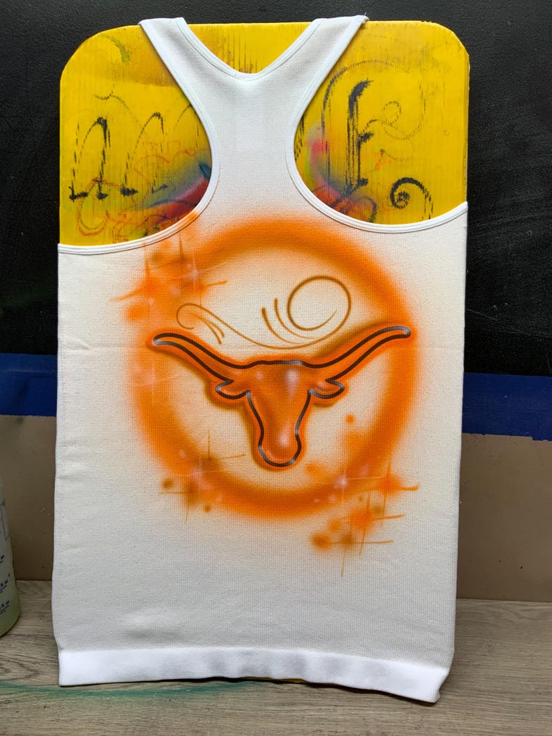 Peut inclure: D&eacute;bardeur blanc avec un logo Longhorn orange et un cercle orange. Le logo est peint &agrave; l'a&eacute;rographe sur le tissu. Le d&eacute;bardeur a une bordure blanche et un dos nageur. Le fond est jaune.