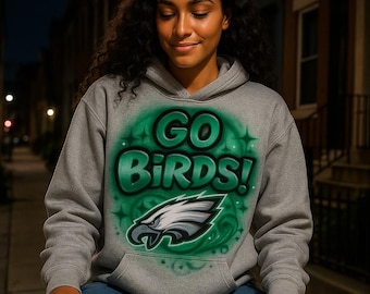 May include: A gray hooded sweatshirt with the words "GO BIRDS!" in green and white, along with a stylized eagle head logo. The design is airbrushed on the front of the sweatshirt.