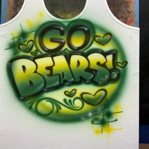 Peut inclure: D&eacute;bardeur blanc avec un motif a&eacute;rographe. Les mots "GO BEARS!" sont en vert et jaune, entour&eacute;s de c&oelig;urs et d'accents verts. Le d&eacute;bardeur a une encolure d&eacute;gag&eacute;e et est fait d'une mati&egrave;re douce.