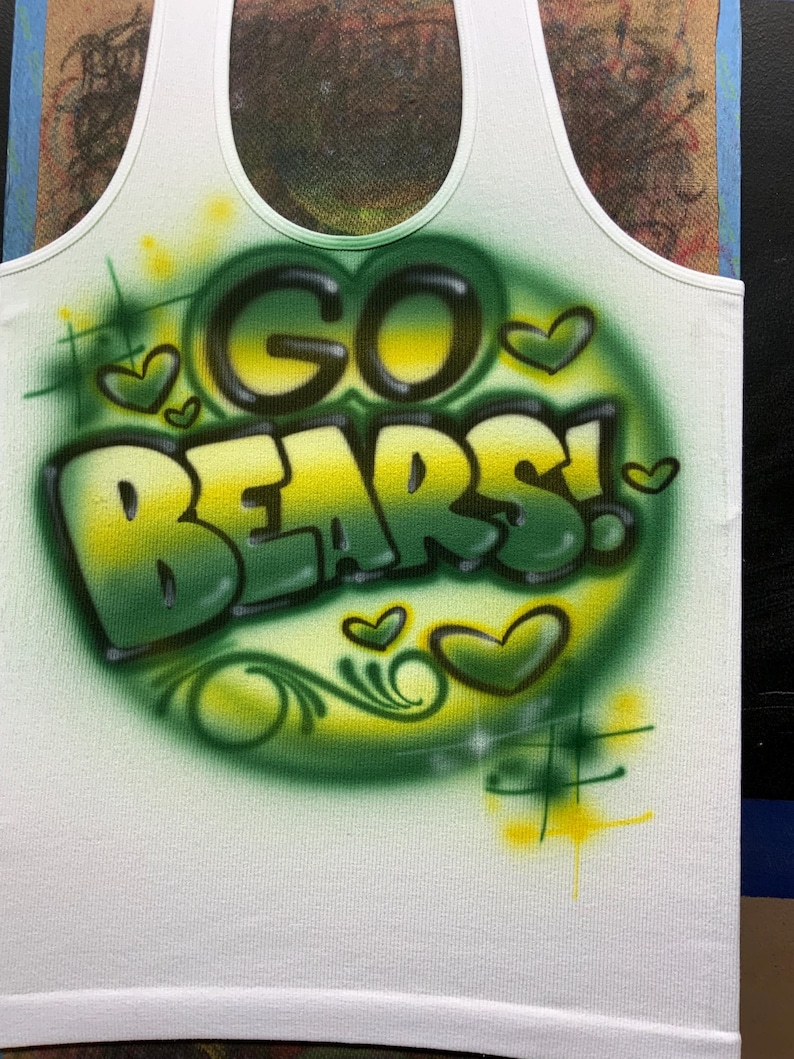 Peut inclure: D&eacute;bardeur blanc avec un motif a&eacute;rographe. Les mots "GO BEARS!" sont en vert et jaune, entour&eacute;s de c&oelig;urs et d'accents verts. Le d&eacute;bardeur a une encolure d&eacute;gag&eacute;e et est fait d'une mati&egrave;re douce.