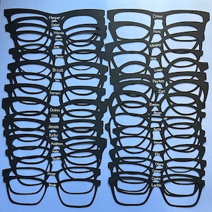 May include: A collection of black die-cut paper eyeglass frames arranged in two vertical columns. Each frame features a unique name printed in white text on the bridge, including Harper, Daley, Wanda, Georgia, Soto, Reese, Brook, Izzy, Iverson, Quinn, Otis, Jessie, Kirby, Addison, Hader, Twain, Finley, Breda, Drew, Flora, Murphy, Nola, Leian, Payton, Zuri, Evelyn, Rowan, Vic, Serra, Sawyer, Ella, Otero, Casper, Cedro, and Larkin.