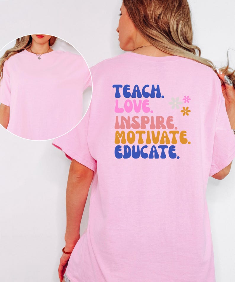 May include: A light pink t-shirt with the words "TEACH. LOVE. INSPIRE. MOTIVATE. EDUCATE." in blue, pink, orange, and yellow lettering. Two small flower graphics are also present. The shirt is a short-sleeved, crew neck style.