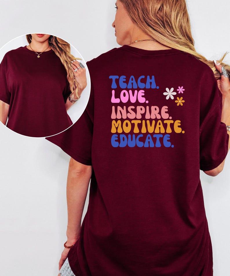 May include: A maroon t-shirt with the words "TEACH. LOVE. INSPIRE. MOTIVATE. EDUCATE." in colorful, retro-style lettering on the back. Two small flower graphics are also present. The shirt has short sleeves and a relaxed fit.