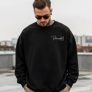 Puede incluir: Una sudadera negra de manga larga con cuello redondo que presenta el texto blanco en cursiva "Patenonkel" seguido de "Est. 2025" impreso en la parte superior izquierda del pecho. La prenda tiene un dise&ntilde;o negro liso con pu&ntilde;os y cuello acanalados.