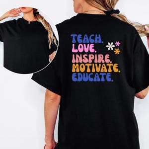 May include: Black t-shirt with the words "TEACH. LOVE. INSPIRE. MOTIVATE. EDUCATE." in a colorful, retro font. Two small flower graphics are next to the text. The shirt is a crew neck and has short sleeves.