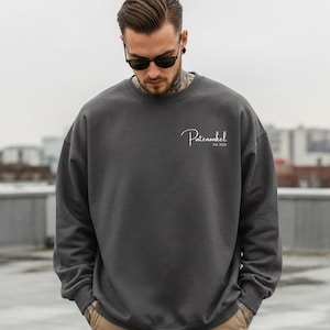 Puede incluir: Una sudadera de cuello redondo en color gris carb&oacute;n oscuro con el texto en cursiva blanca Patenonkel y el texto m&aacute;s peque&ntilde;o Est. 2025 impresos en la parte superior izquierda del pecho. Tiene mangas largas con pu&ntilde;os y cuello acanalados.