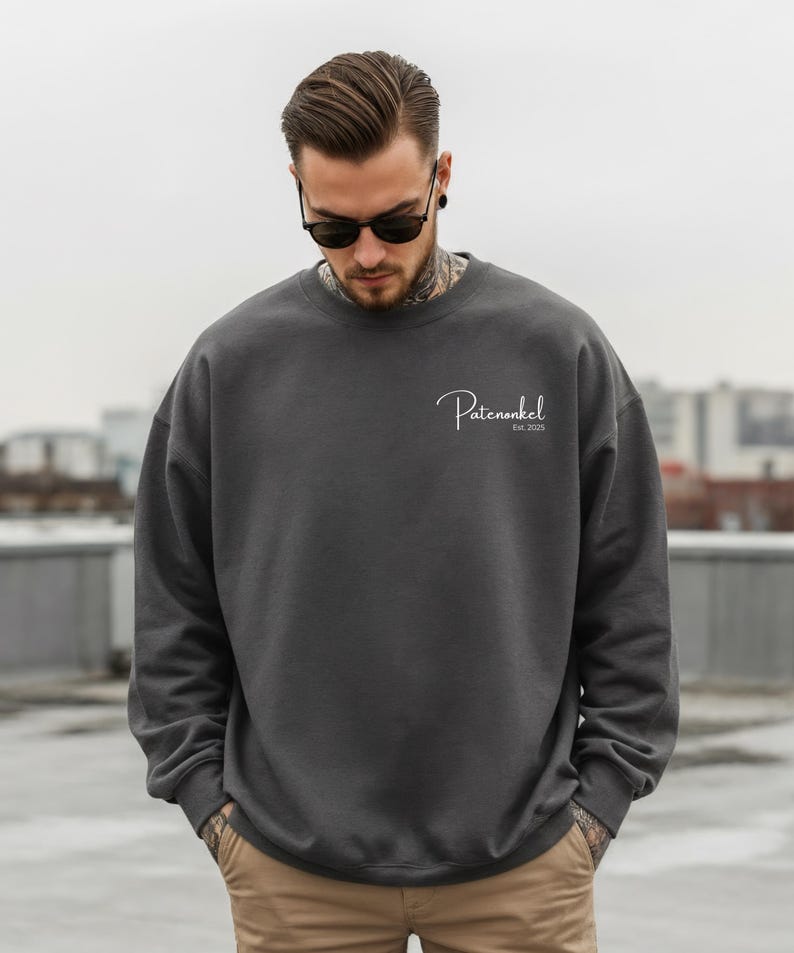 Puede incluir: Una sudadera de cuello redondo en color gris carb&oacute;n oscuro con el texto en cursiva blanca Patenonkel y el texto m&aacute;s peque&ntilde;o Est. 2025 impresos en la parte superior izquierda del pecho. Tiene mangas largas con pu&ntilde;os y cuello acanalados.