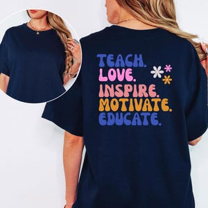 May include: Navy blue t-shirt with the words "TEACH. LOVE. INSPIRE. MOTIVATE. EDUCATE." in a retro font. The back of the shirt also features two small flower graphics. A casual, comfortable tee for teachers.