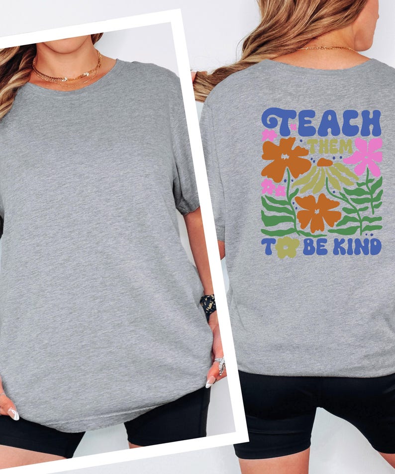 May include: A heather gray t-shirt with the words "TEACH THEM TO BE KIND" printed on the back, along with a floral design in orange, pink, and green. The shirt is a casual style.