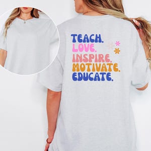May include: Light gray t-shirt with the words "TEACH. LOVE. INSPIRE. MOTIVATE. EDUCATE." in blue, pink, orange, and blue lettering. Two small flower graphics are next to the word "INSPIRE". The shirt is a short-sleeved, crew neck style.