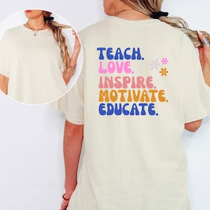 May include: Cream-colored t-shirt with the words "TEACH. LOVE. INSPIRE. MOTIVATE. EDUCATE." in blue, pink, orange, and blue lettering. Two small flower graphics are also present. The shirt is a casual style.