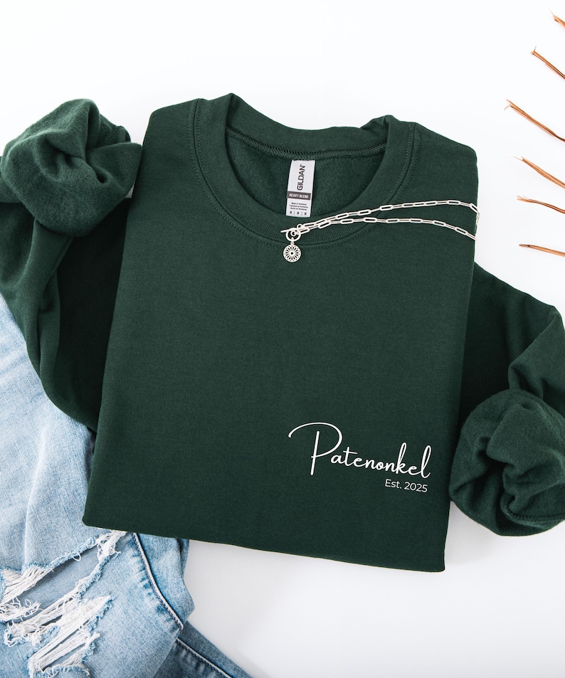 Puede incluir: Una sudadera de cuello redondo en color verde bosque oscuro con el texto en cursiva blanca Patenonkel y el texto impreso Est. 2025 en la parte inferior derecha. Un collar de cadena plateada con un colgante circular descansa en el cuello.
