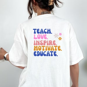 May include: White t-shirt with the words "TEACH. LOVE. INSPIRE. MOTIVATE. EDUCATE." in blue, pink, orange, and blue lettering. Two small flower graphics are to the right of the text. The shirt is a casual style.