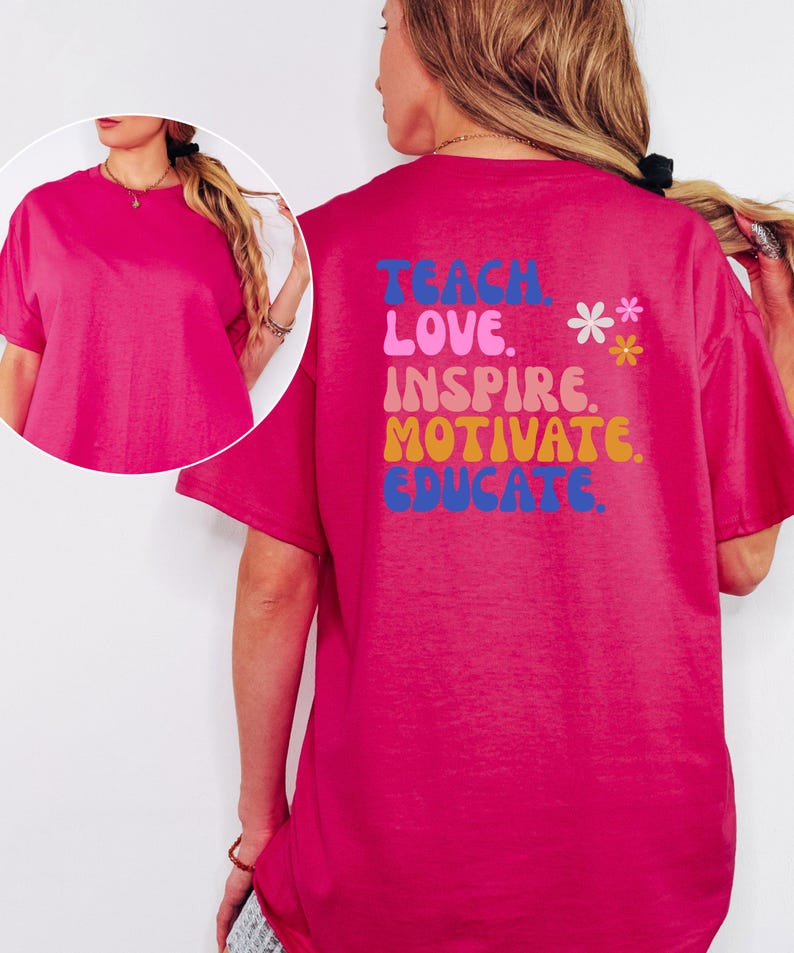 May include: A vibrant fuchsia t-shirt with short sleeves. The back of the shirt features the words "TEACH, LOVE, INSPIRE, MOTIVATE, EDUCATE" in a colorful, retro font, with two small flower graphics. A casual, comfortable tee.