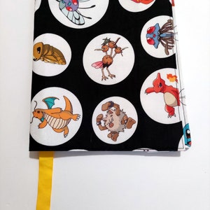 May include: Black book cover with a white background and a repeating pattern of Pokemon characters in white circles. The book cover has a yellow bookmark.