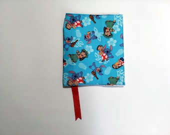 May include: A blue book cover featuring a repeating pattern of cartoon characters, pineapples, and tropical flowers. The cover has a red ribbon bookmark. The book cover is on a white surface.