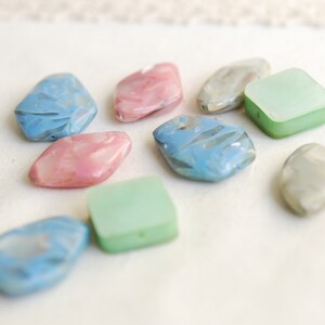 May include: Assortment of colorful, translucent, and opaque glass beads in various shapes, including squares, rectangles, and irregular shapes. The beads are in shades of blue, green, and pink.