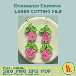 May include: A pair of engraved earrings with a laser-cut design. The earrings feature a pink floral shape with green leaves. The text "ENGRAVED EARRING LASER CUTTING FILE" is at the top. The image also includes the text "SVG PNG EPS PDF INSTANT DIGITAL DOWNLOAD".
