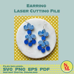 May include: A pair of blue and white cloud-shaped earrings with dangling blue circles. The earrings are displayed on a white circular surface against a light blue background. Text at the top reads "EARRING LASER CUTTING FILE".