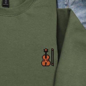 May include: Olive green sweatshirt with a small embroidered violin and bow design on the chest. The crew neck sweatshirt is made of a soft material. The design is in shades of orange and brown.