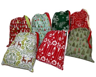 May include: Six Christmas gift bags with various holiday patterns. The bags are made of fabric and have a drawstring closure. The patterns include red and green trees, reindeer, ornaments, and a Santa Claus design.