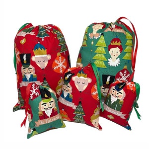 May include: Set of five red and green drawstring gift bags with a Nutcracker theme. The bags feature illustrations of a Nutcracker soldier, a mouse king, a Christmas tree, and a snowflake. The bags are made of fabric and have a drawstring closure.