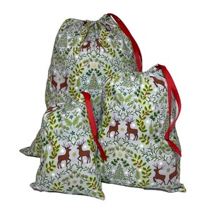 May include: Three drawstring gift bags in varying sizes. The bags feature a light gray background with a repeating pattern of brown deer, green foliage, and white accents. Each bag has a red ribbon drawstring.