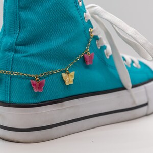 May include: A pair of turquoise high-top sneakers with a white sole and a gold chain ankle bracelet with pink and yellow butterfly charms.