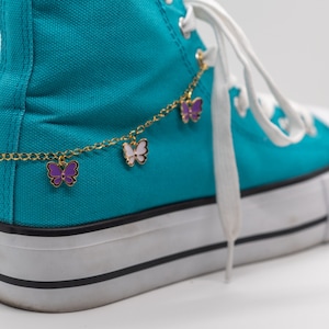 May include: A pair of turquoise sneakers with a gold chain and butterfly charms around the ankle.