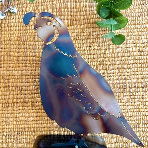 May include: A metal sculpture of a quail with a brown, blue and purple patina. The quail is standing on a black metal base.