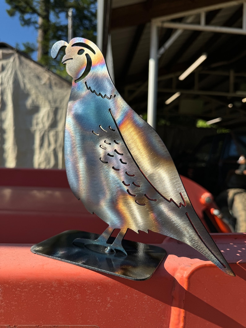 May include: A metal sculpture of a quail with an iridescent finish. The sculpture is standing on a black metal base.