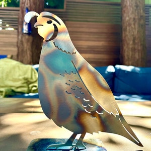 May include: A metal sculpture of a quail with a brown and blue patina finish. The sculpture is standing on a black metal base.