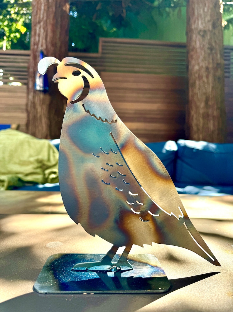 May include: A metal sculpture of a quail with a brown and blue patina finish. The sculpture is standing on a black metal base.