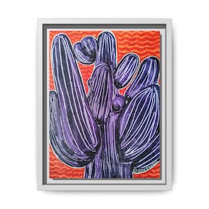 May include: A framed painting of a purple cactus with white stripes against an orange background. The artwork is in a white frame. The cactus has multiple arms and a rounded shape. The background has a wavy pattern.