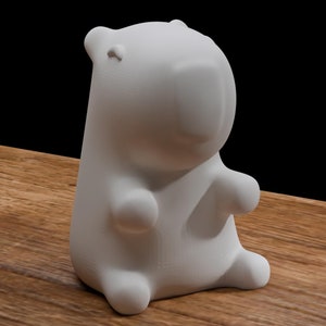 May include: A white ceramic figurine of a cartoon bear sitting on a wooden surface.