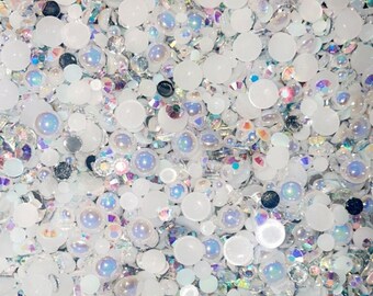 May include: A close-up of a variety of white and iridescent rhinestones and pearls. The rhinestones are in different shapes and sizes, and the pearls are round and white.