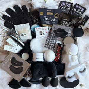 Puede incluir: Una caja de regalo llena de artículos de cuidado personal. Incluye una mascarilla negra, mascarillas para los ojos, una mascarilla de carbón, bolsitas de té, una barra de chocolate Mars y una máscara para dormir. La caja también contiene una bomba de baño blanca, crema facial y un pin de panda.