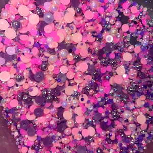 Peut inclure: Un grand assortiment de strass irisés roses et violets de différentes tailles et formes. Les strass sont dans un bol et semblent être en vrac.