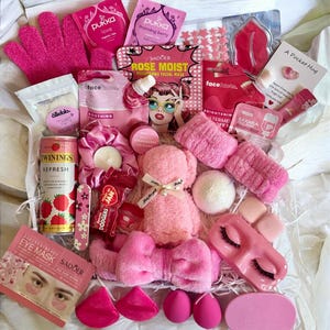 May include: A pink gift box containing beauty and self-care products. Items include face masks, a plush bear, bath bombs, eye mask, gloves, lip balm, tea, and other pink accessories. A collection of pampering treats.