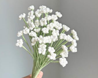 May include: A bouquet of white crochet flowers with pearl accents and green stems. The stems are bundled together and wrapped in green thread. The flowers are held in a hand. The logo "YEPVIVI FLORAL" is in the bottom right corner.