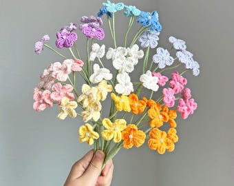 May include: A bouquet of handmade crochet flowers in various colors, including pink, yellow, orange, and blue. Each flower has a small bead in the center. The stems are green, and the bouquet is held in a hand.