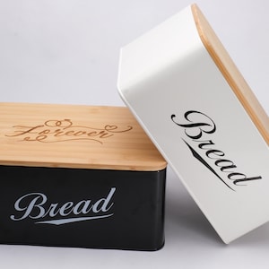 May include: Two rectangular bread boxes with wooden lids. One box is black with "Bread" in white script, the other is white with "Bread" in black script. The black box lid has "Forever" engraved on it.