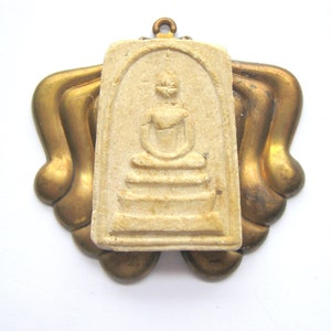 May include: A white ceramic pendant with a raised image of a seated Buddha figure. The pendant is attached to a gold-colored metal frame.