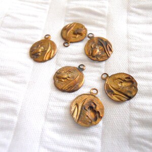 May include: Six antique gold-toned metal charms with a raised design of a frog on each. The charms have a loop at the top for attaching to a necklace or bracelet.