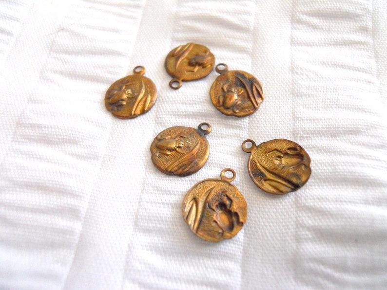 May include: Six antique gold-toned metal charms with a raised design of a frog on each. The charms have a loop at the top for attaching to a necklace or bracelet.