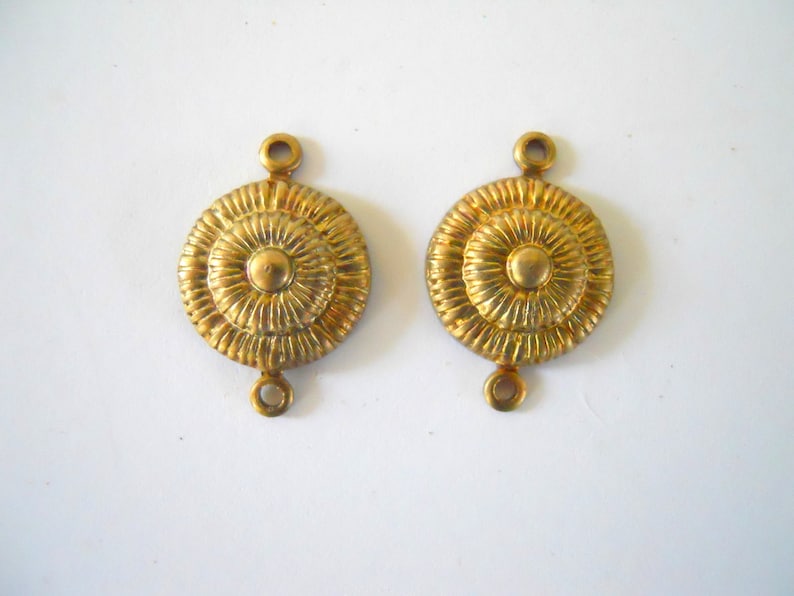 May include: Two gold-toned metal connector pieces with a circular design. Each piece has a raised, textured centre with a smaller circle in the middle. The pieces have two small loops on the top and bottom.