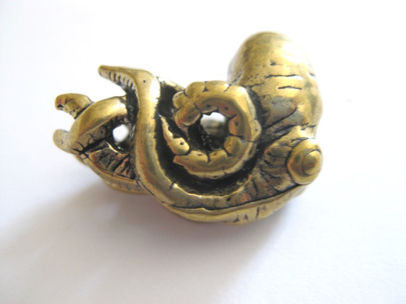 May include: A gold-colored metal sculpture of a curled octopus with detailed texture. The sculpture is a unique and intricate piece of art.