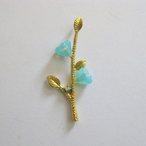 May include: A gold-tone branch with three light blue flower accents and a single clear rhinestone.
